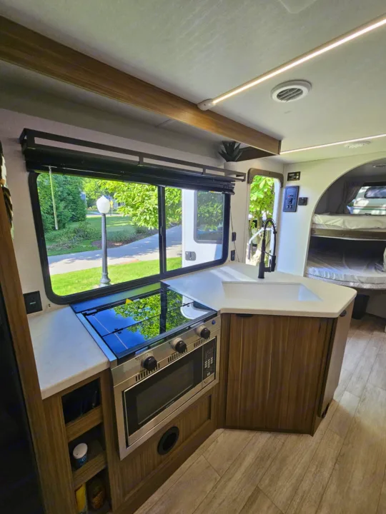 Modern RV rental interior: kitchen with sink, stove, window view, and bunk beds.. Forest River 26Ice 2025