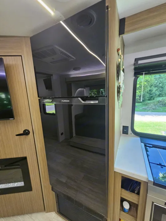 Spacious, modern RV rental interior featuring a large black refrigerator, well-equipped kitchen, and cozy living area.. Forest River 26Ice 2025