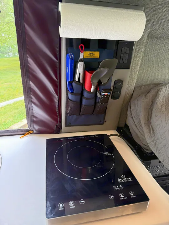 Compact kitchen setup in an RV rental, featuring an induction cooktop, wall organizer for utensils, paper towels, and power outlets.. Storyteller Overland Storyteller Overland Class B 2023