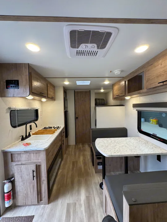 Bright RV rental interior: modern kitchen with stove, sink, and counter, plus a comfortable dinette. Features wood-look flooring.. Gulf Stream Coach Enlighten 17bh 2025