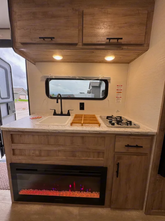 RV rental: Bright kitchen with sink, two-burner stove, overhead cabinets, and a built-in electric fireplace.. Gulf Stream Coach Enlighten 17bh 2025