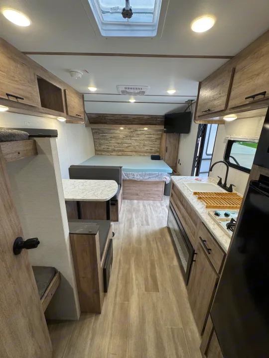 Modern RV rental interior with kitchen, dinette, and cozy bed. Features include overhead storage & wood-look flooring.. Gulf Stream Coach Enlighten 17bh 2025