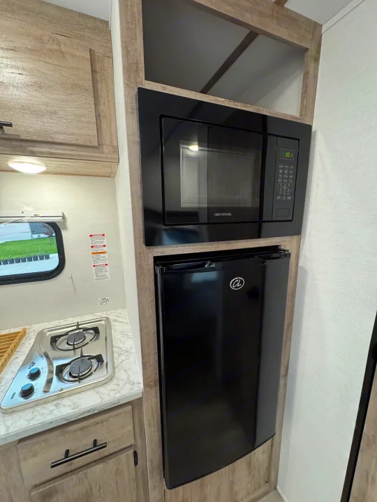 Functional RV rental kitchen with wood cabinets, a Greystone microwave, compact refrigerator, and two-burner stove.. Gulf Stream Coach Enlighten 17bh 2025