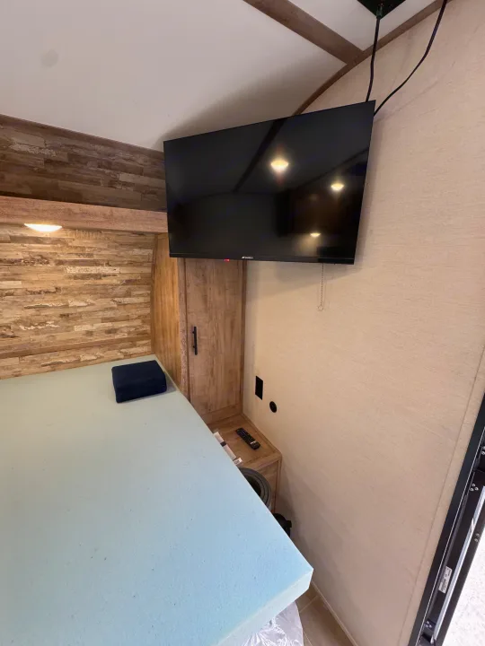 Inside an RV rental: a compact bedroom features a light blue mattress, wall-mounted TV, and wooden cabinet storage.. Gulf Stream Coach Enlighten 17bh 2025
