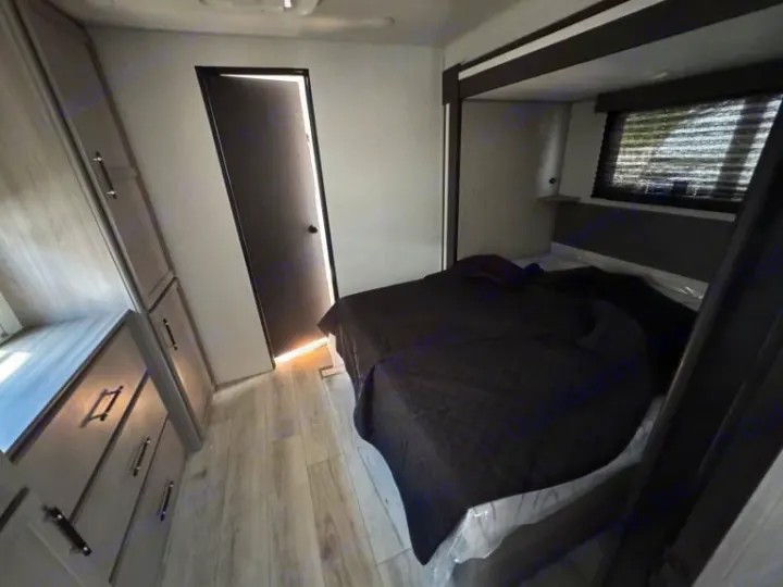 Step into this modern RV rental bedroom, featuring a comfy bed with dark bedding, built-in cabinets, and wood-look flooring.. evergreen sun valley 2015