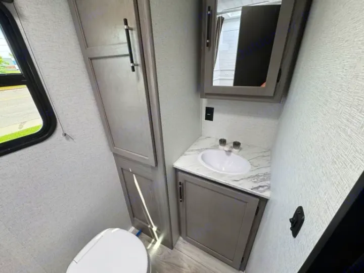 Modern RV rental bathroom featuring a toilet, sink, mirror, and ample storage for comfortable travels.. evergreen sun valley 2015