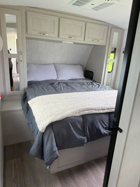 Step into comfort! This modern RV rental bedroom features a cozy bed with gray bedding, overhead cabinets, and a mirrored wardrobe.. Cruiser RV Shadow Cruiser 2025