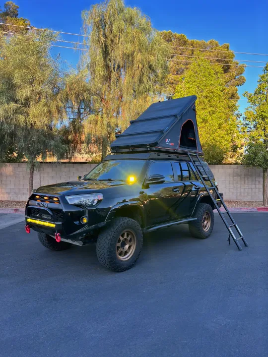Adventure-ready black Toyota 4Runner with a rooftop tent and ladder, perfect as an RV rental for off-road camping and overlanding.. Toyota 4Runner 2020