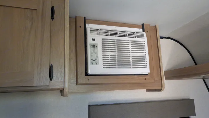RV rental interior: A white window AC unit is integrated into light wood cabinetry, with controls visible, providing cooling.. Keystone Coleman 13B 2025