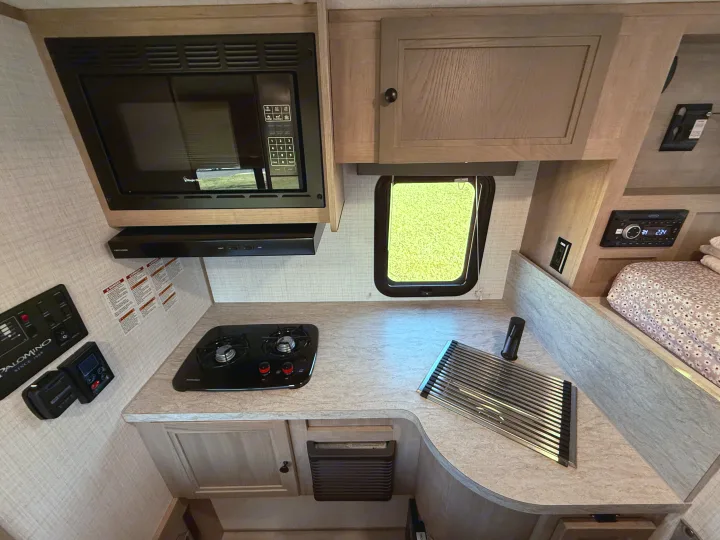 Compact RV rental kitchen featuring microwave, two-burner stove, sink area, and controls. Ready for your next adventure!. Palomino Backpack Edition 2026