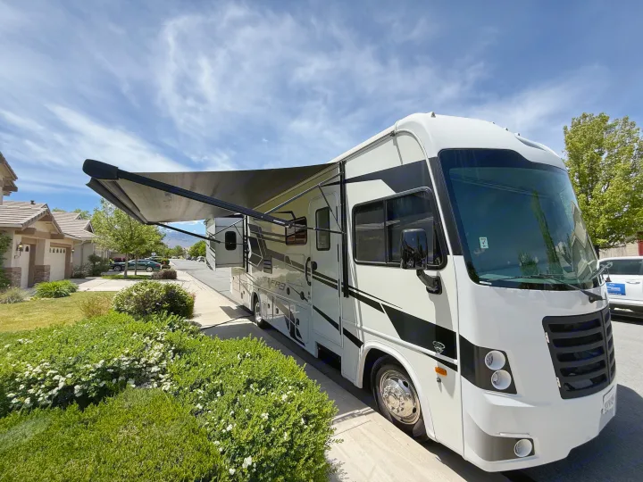A white RV rental, with its awning extended and slide-out deployed, parked on a sunny residential street. Ready for adventure!. FR3 FR3 Motorhome 2023