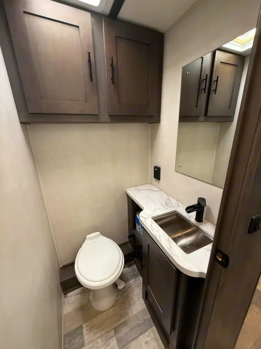 Clean and modern RV bathroom in an rv rental, featuring a compact toilet, vanity with sink, and overhead storage.. FR3 FR3 Motorhome 2023