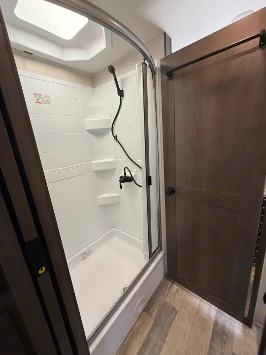 RV rental ready: a clean, compact shower interior with modern black fixtures, white tiled walls, and an adjacent dark wood door.. FR3 FR3 Motorhome 2023
