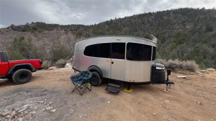 Aluminum travel trailer RV rental & red truck parked for scenic camping.. Airstream Basecamp 2024