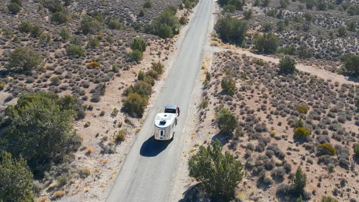 Aerial view: An RV rental is towed on a winding desert road, surrounded by sparse brush. Perfect for remote travel and road trips.. Airstream Basecamp 2024