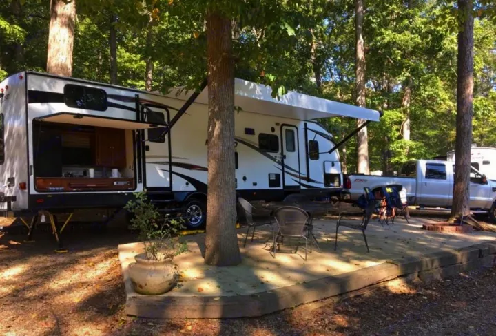 RV rental at a shaded campsite, featuring a travel trailer with open outdoor kitchen, patio area, and pickup truck.. Heartland RVs Mallard 2018