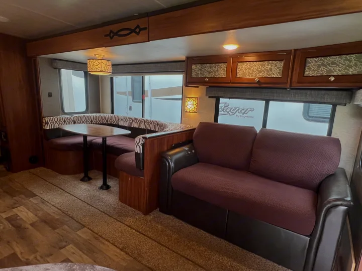 RV rental interior showcasing a U-shaped dinette, comfortable sofa, wood cabinetry, and large windows.. Heartland RVs Mallard 2018
