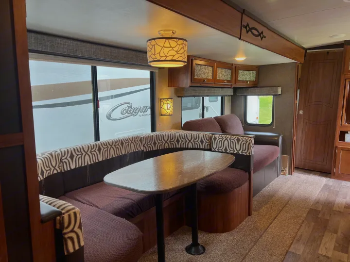 Spacious RV rental interior featuring a cozy dinette with patterned cushions, overhead cabinets, and large windows.. Heartland RVs Mallard 2018