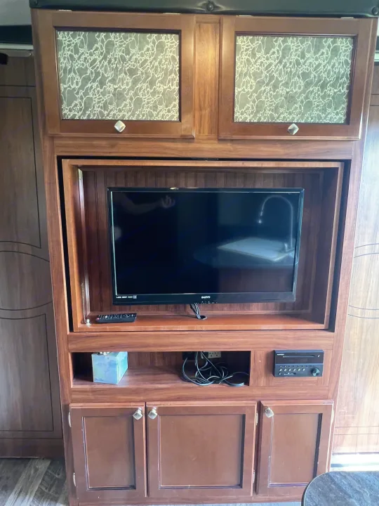 RV rental interior: A built-in wood entertainment center with a TV, remote, audio unit, and frosted-glass cabinets.. Heartland RVs Mallard 2018