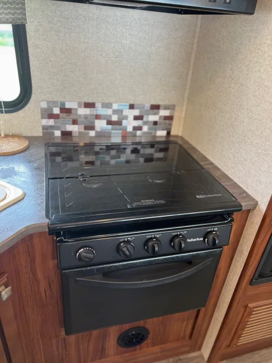 RV rental kitchen: Black Suburban stove and oven with glass cooktop and a decorative mosaic tile backsplash.. Heartland RVs Mallard 2018