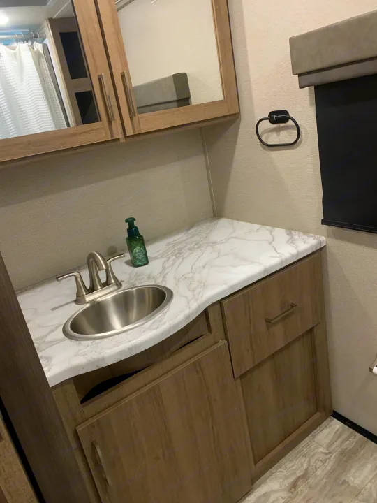 RV rental bathroom vanity featuring a modern sink, mirror, and wood cabinets. A compact and functional space.. Grand Design Imagine XLS 2022