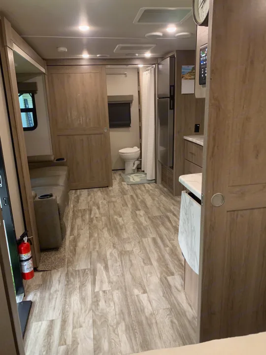 Spacious RV rental interior: lounge area, full bath, kitchen, and modern wood-look flooring. Clean and bright.. Grand Design Imagine XLS 2022