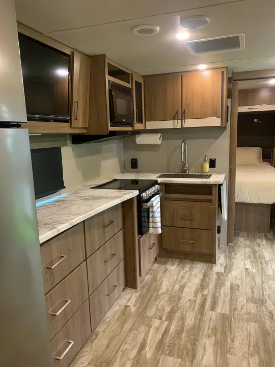 Modern rv rental with full kitchen (stove, microwave) and cozy bedroom, featuring light wood cabinets and marble counters.. Grand Design Imagine XLS 2022