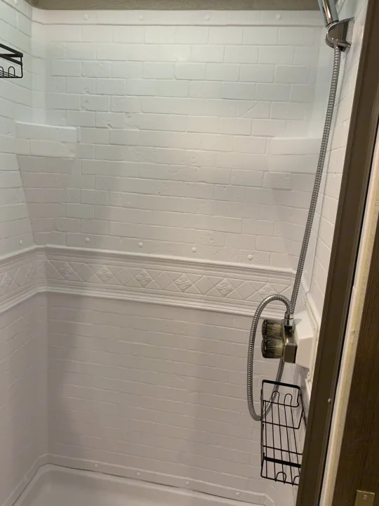 Inside an RV rental: a pristine shower with white faux-brick walls, flexible shower head, and soap caddy.. Grand Design Imagine XLS 2022