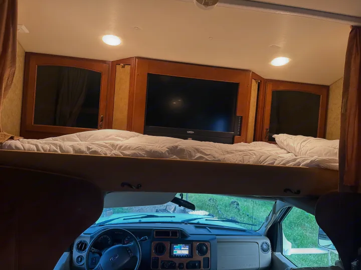 Spacious RV rental interior with an overhead bunk bed, entertainment TV, and the driver's cab.. Jayco Greyhawk 2011