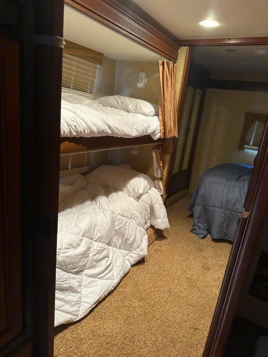 Spacious RV rental bedroom featuring comfy bunk beds with white linens and an additional bed with blue bedding, perfect for family trips.. Jayco Greyhawk 2011