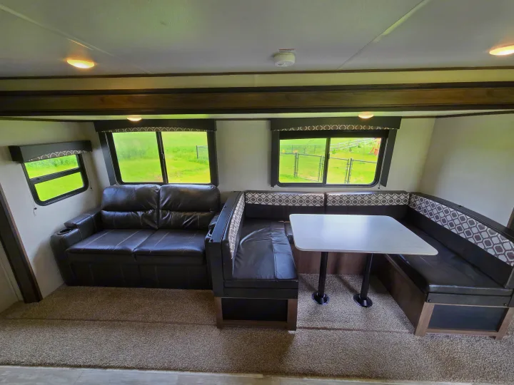 Spacious RV rental interior with a comfy faux leather couch, U-shaped dinette, and large windows revealing green outdoor views.. Avenger Avenger Trailer 2021
