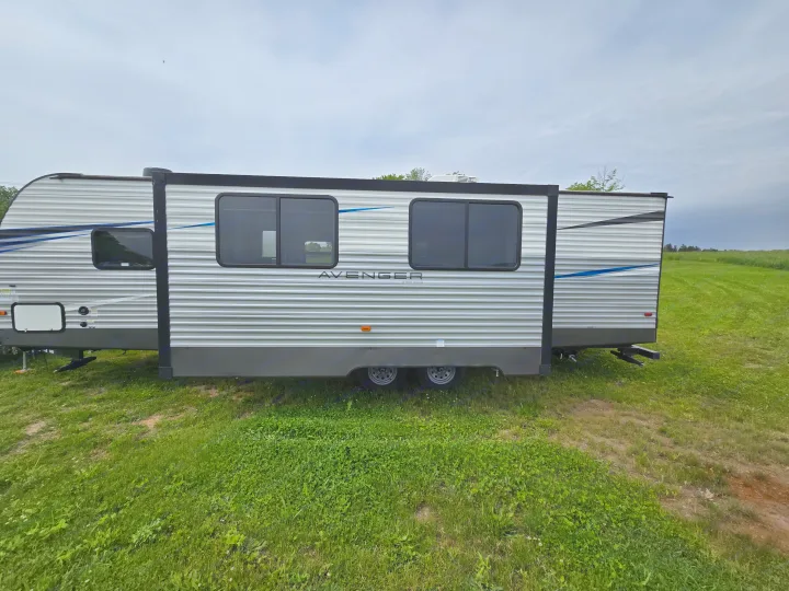 A modern "Avenger" travel trailer (rv rental) with a slide-out, parked on a grassy field on a cloudy day.. Avenger Avenger Trailer 2021