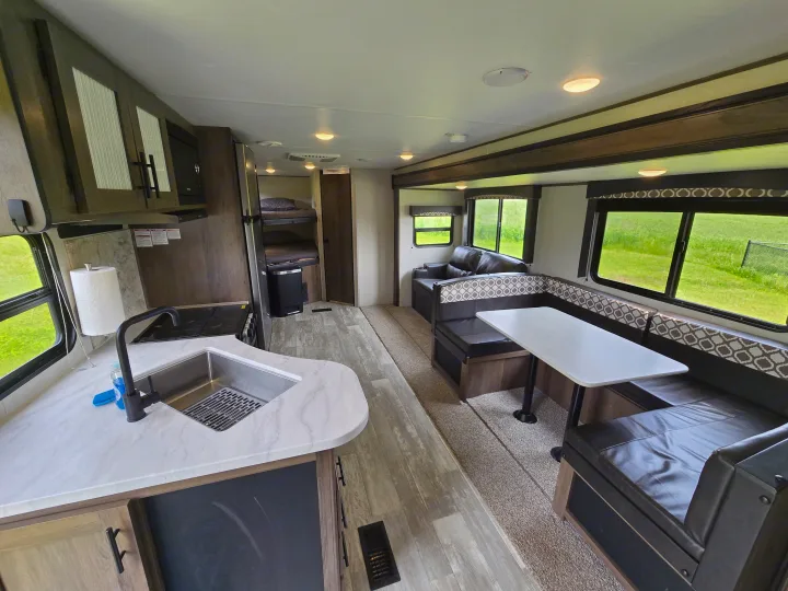 Clean rv rental interior: kitchen with sink, U-shaped dinette, sofa, and bunk beds. Perfect for road trips.. Avenger Avenger Trailer 2021