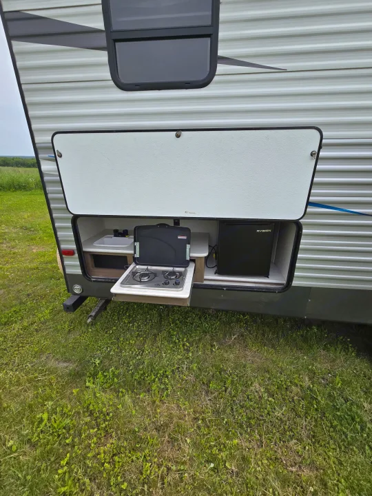 This rv rental features a side compartment open to reveal a full outdoor kitchen with a sink, stove, and mini-fridge, ideal for camping adventures.. Avenger Avenger Trailer 2021