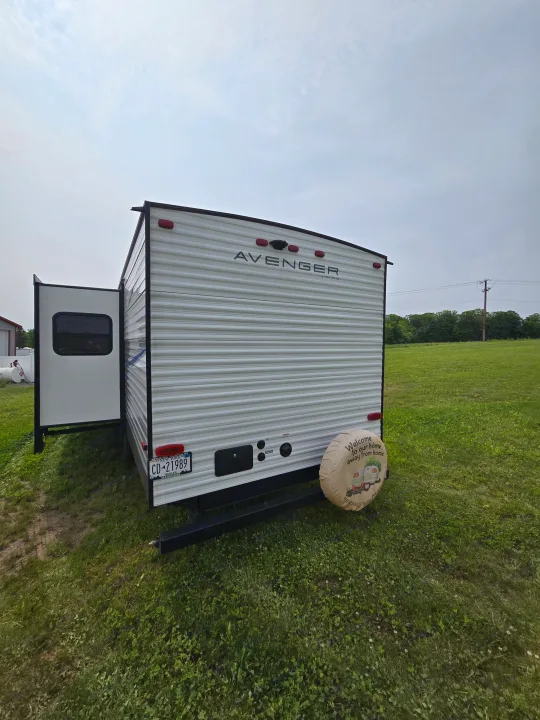 Avenger travel trailer rv rental. Rear view of the white RV with an extended slide-out, parked in a green field.. Avenger Avenger Trailer 2021