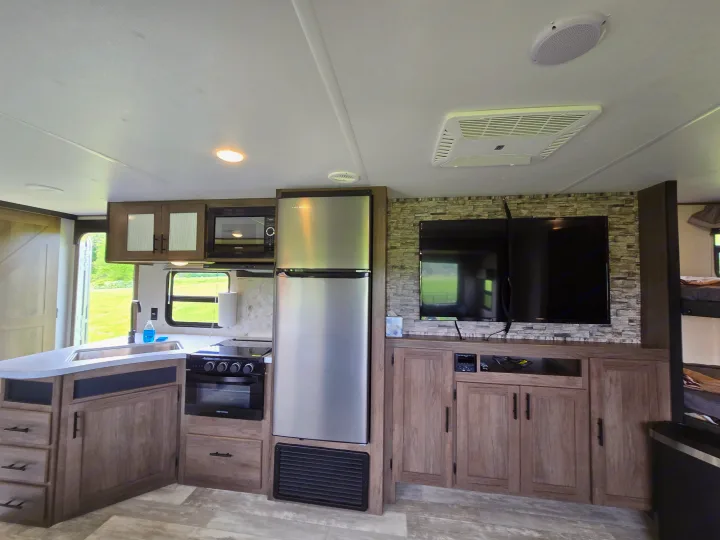 Spacious rv rental interior showing a modern kitchen with a large fridge, stove, microwave, and a TV entertainment area.. Avenger Avenger Trailer 2021