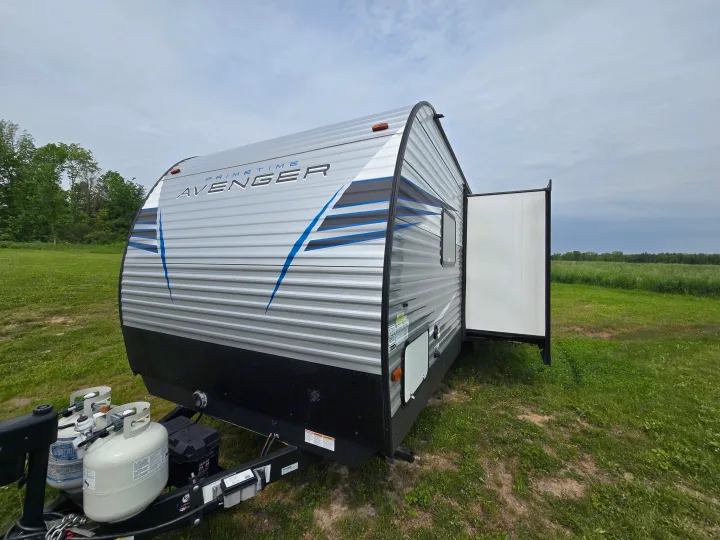 Avenger travel trailer for rv rental, parked in a grassy field with an open ramp door under a cloudy sky.. Avenger Avenger Trailer 2021