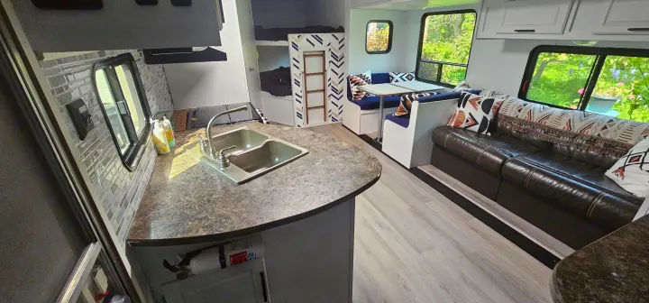 Spacious and modern RV rental interior, showing a kitchen with sink, dining booth, brown sofa, and bunk beds.. Crossroads RV Z-1 2015