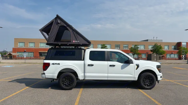 A white Ford F-150 pickup truck with a black truck cap and open rooftop tent, ready for camping. Think RV rental for adventure!. Ford Ford F150 2025