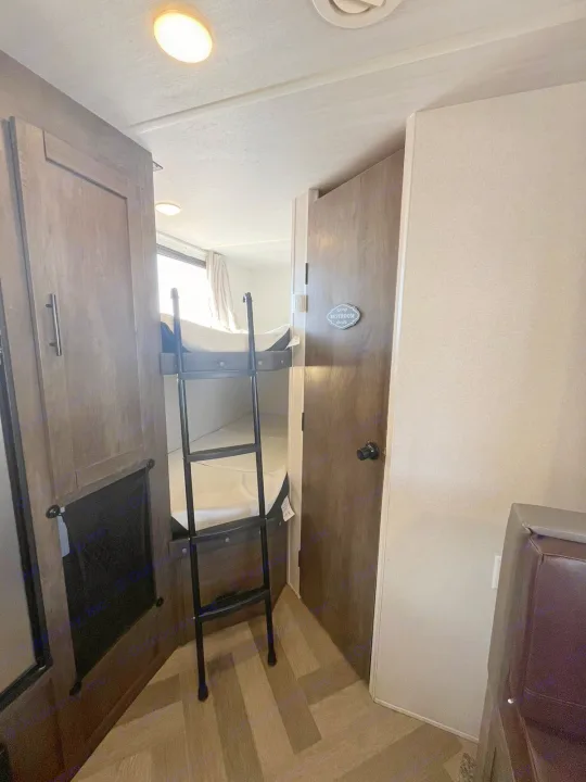 Inside an RV rental: Looking toward the back, you see bunk beds with a ladder on the left, and a restroom door on the right.. Forest River EVO 2021