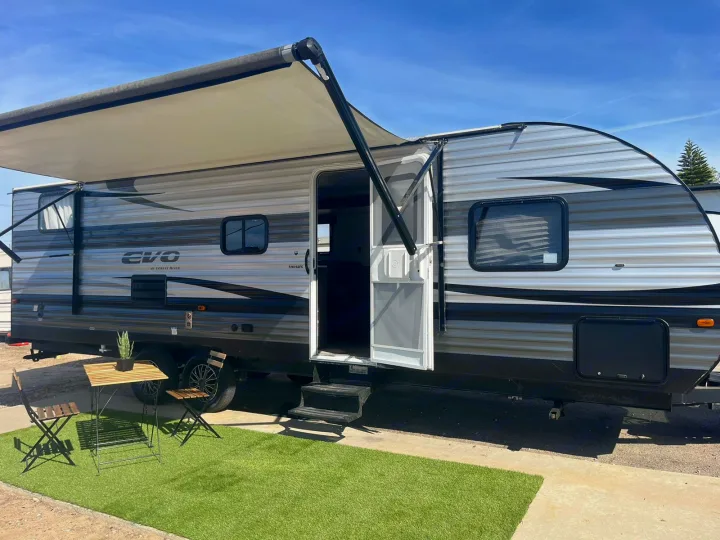 Spacious RV rental set up for a relaxing day. This travel trailer features an extended awning, outdoor seating, and easy step-in access.. Forest River EVO 2021