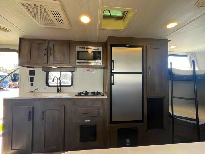 Interior of a modern RV rental, featuring a full kitchen with microwave, fridge, sink, stovetop, and bunk beds.. Forest River EVO 2021