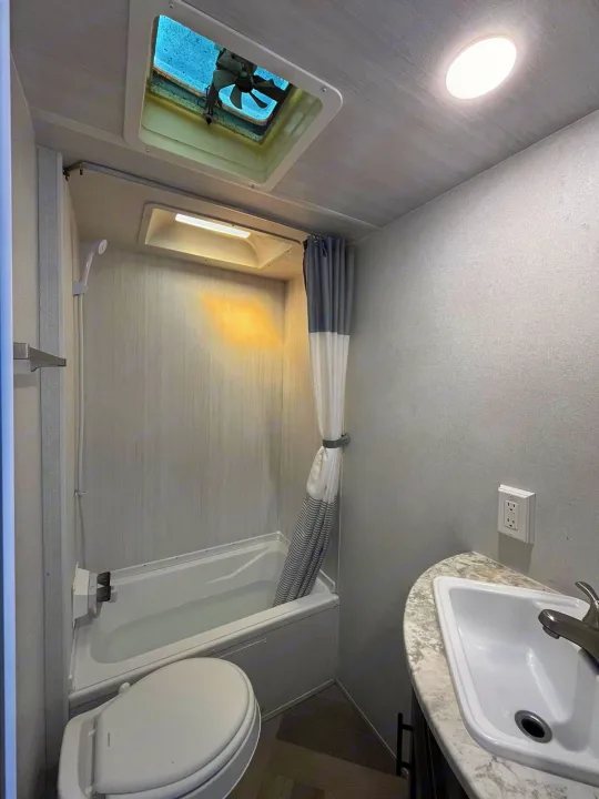 A compact RV rental bathroom featuring a small tub filled with water, toilet, sink, and overhead fan.. Forest River EVO 2021