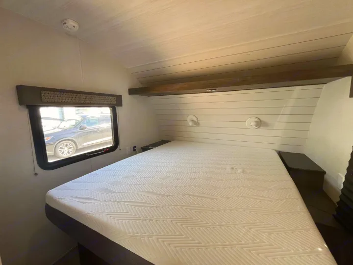 Comfortable RV rental bedroom featuring a large bed with a patterned mattress, shiplap headboard, and wall lights.. Forest River EVO 2021