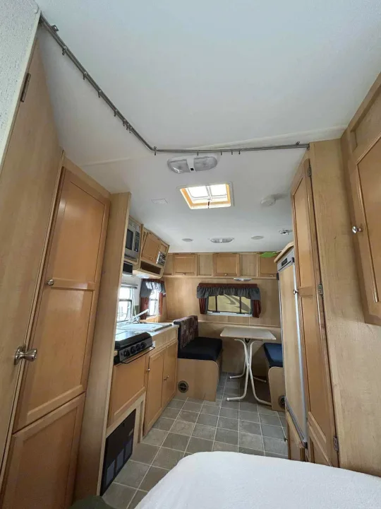 Explore this cozy rv rental interior featuring light wood cabinetry, a full kitchen with stove and sink, and a dining booth.. R-Vision Trail-Lite Trail-Cruiser 2004