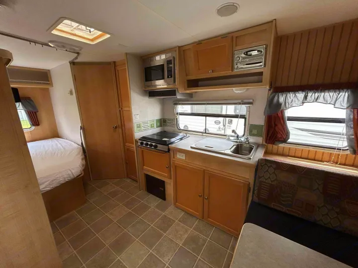 RV rental interior featuring a compact kitchen with microwave, sink, and stovetop, plus a bed and dining area.. R-Vision Trail-Lite Trail-Cruiser 2004