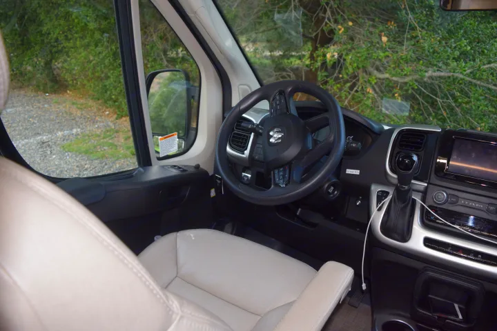 Inside an rv rental, featuring the cockpit with a Ram steering wheel, dashboard, gear shift, and serene natural view.. Thor Sequnce 2023