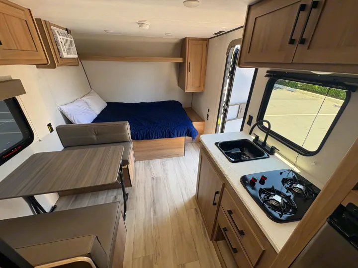 Explore this RV rental's interior: a comfortable bed, compact kitchen with sink & stove, and cozy dinette area.. Keystone RV Coleman 2025