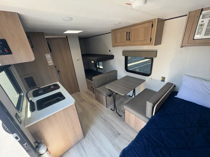 Inside an RV rental: full view of the compact kitchen, dining area, bunk beds, and main sleeping space, ready for travel.. Keystone RV Coleman 2025