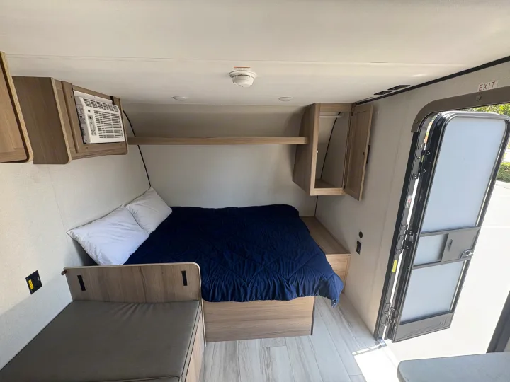 RV rental interior features: a cozy bedroom with blue bedding, AC, storage, and a versatile sitting area.. Keystone RV Coleman 2025